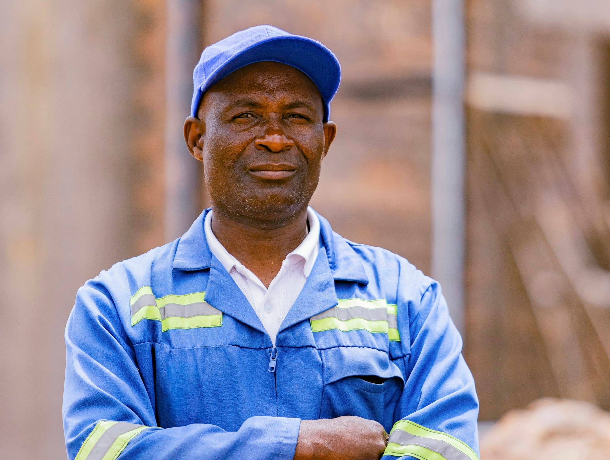 Portrait of a worker in blue reflective overalls and a cap, arms folded.